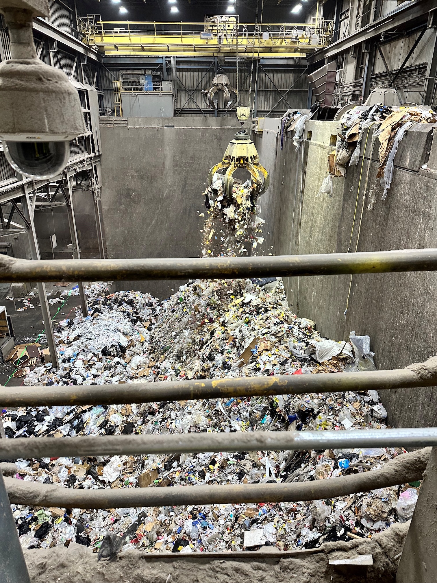 A view of the trash floor inside HERC with a claw scooping trash to deliver to the burners